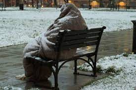 na zdjęciu osoba bezdomna marznąca na ławce w parku